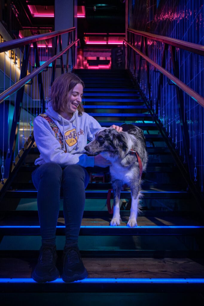 Kvinne med hund på trapp under neonbelysning, moderne atmosfære.