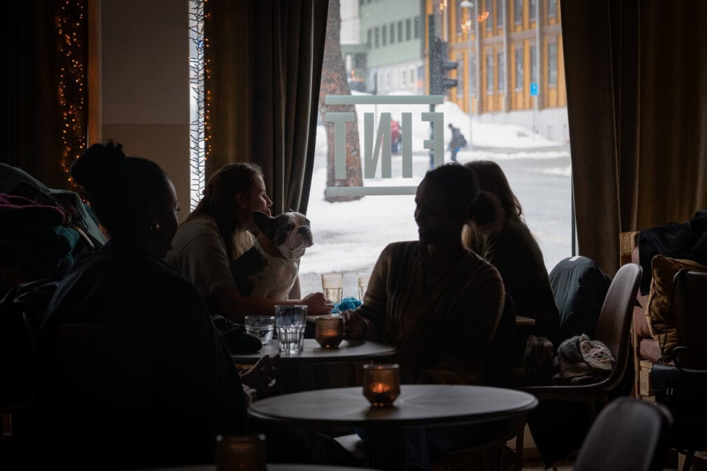 Venner og hund nyter kveldsstemning på kafé med utsikt til snødekt bylandskap.