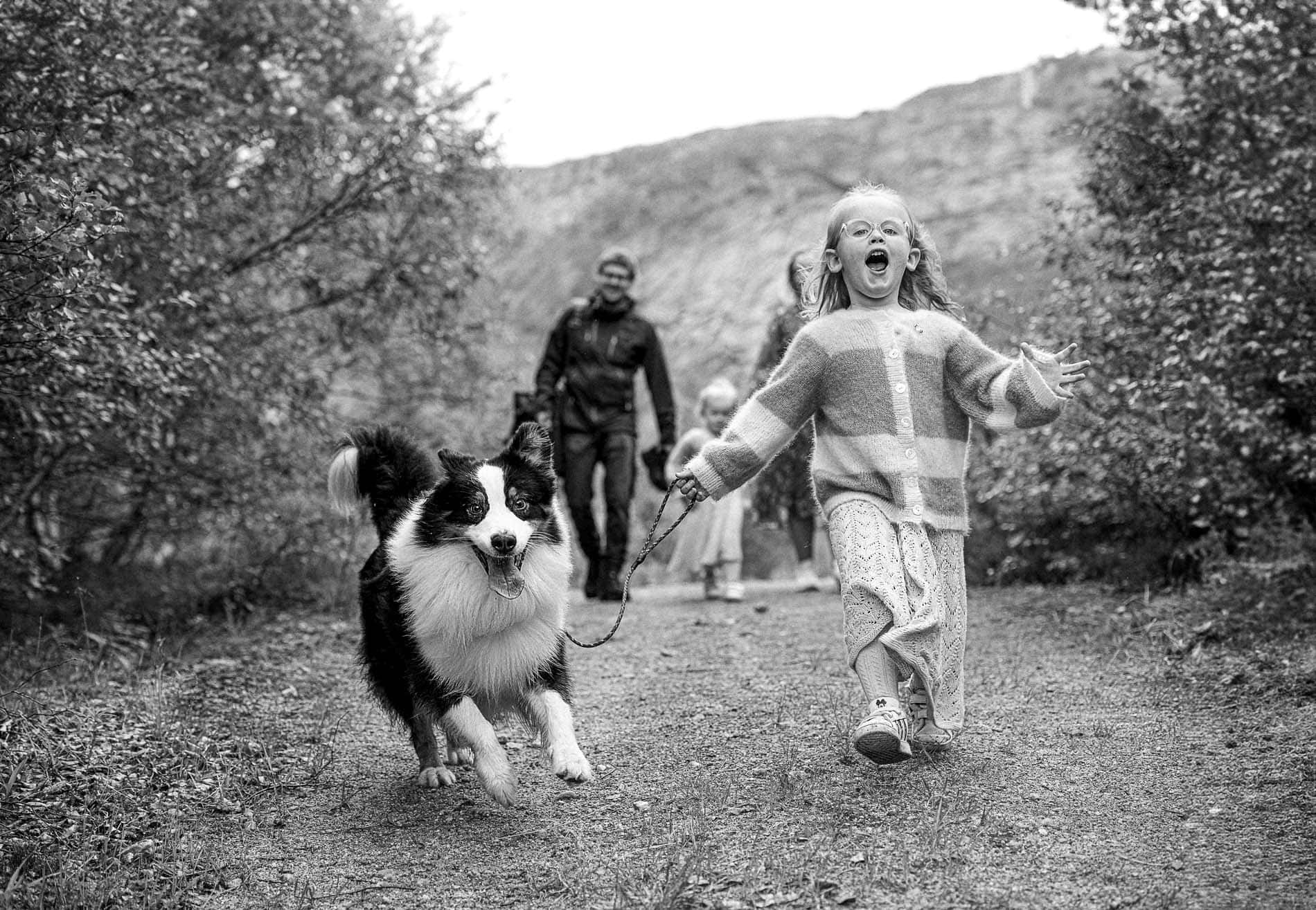 Familie med barn og hund på tur i naturen, smilende og glade.