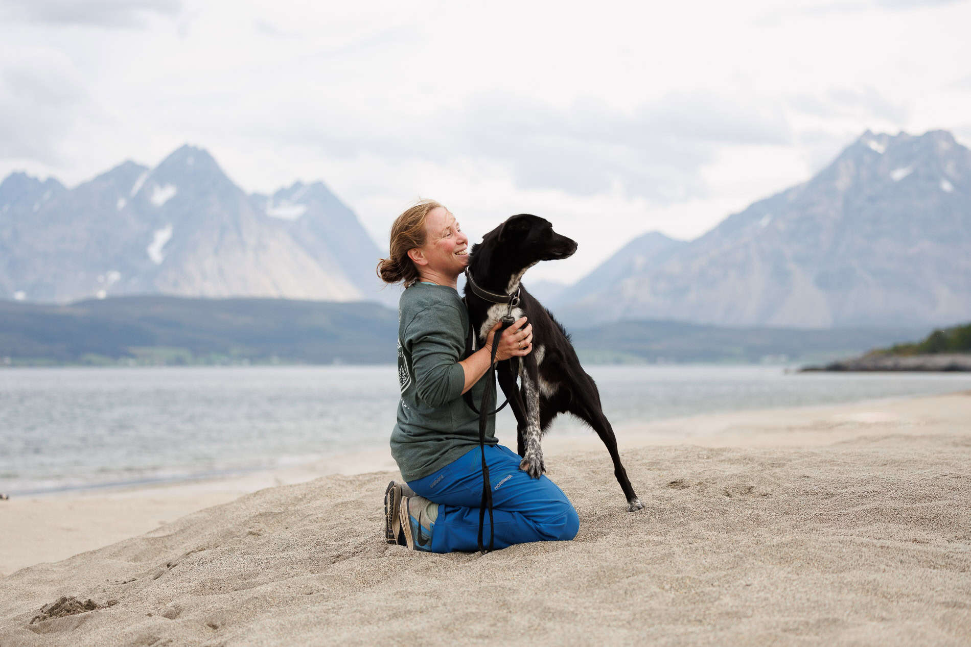 Familie med hund på stranden med fjell i bakgrunnen, vakker natur.